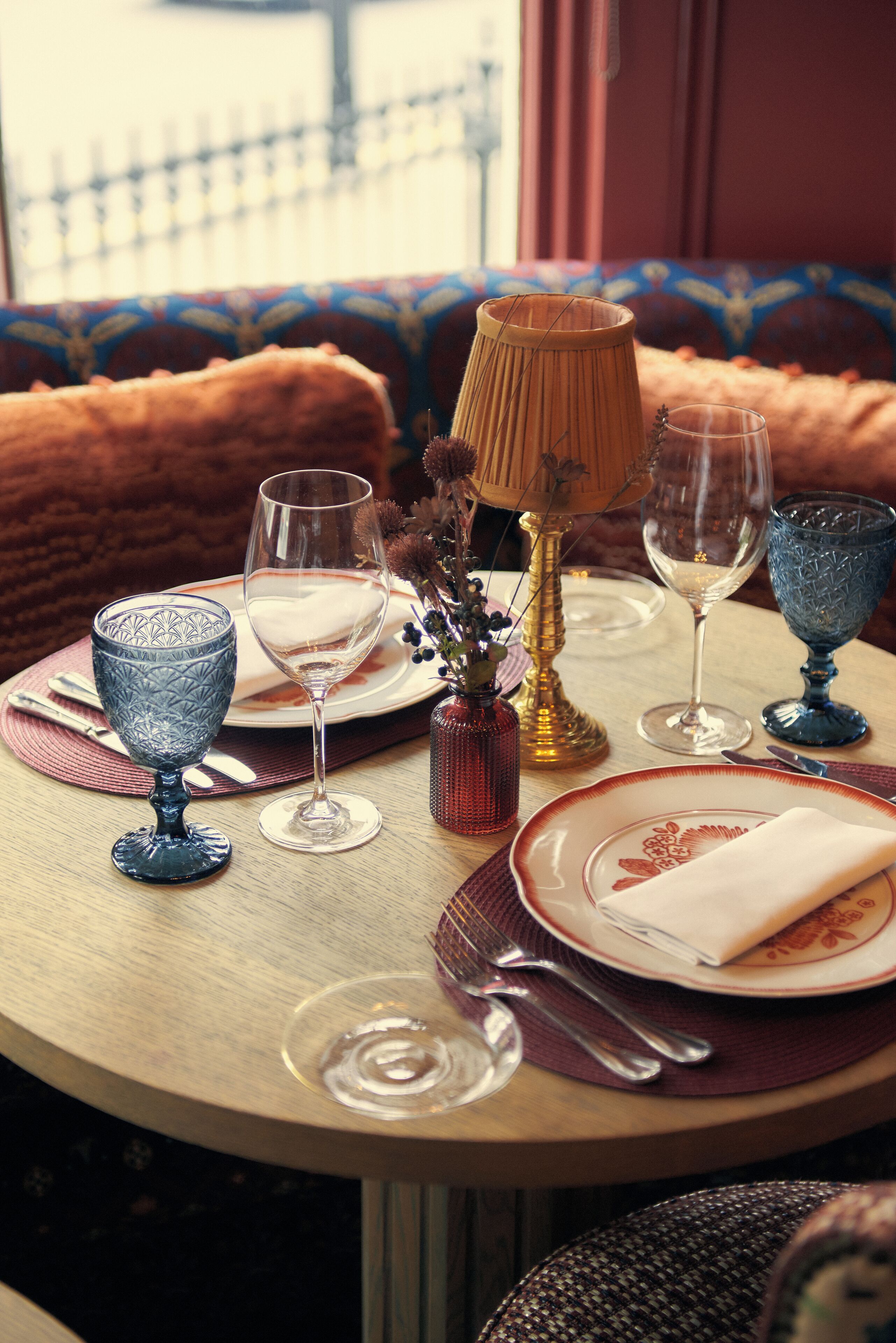 A round table set with dinnerware, glasses, and a lamp.