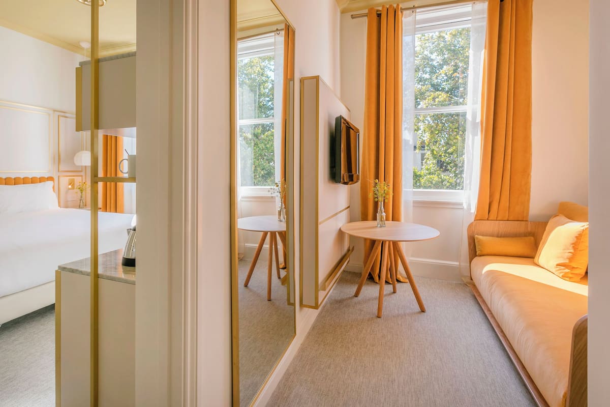 Ein Hotelzimmer mit Bett, einer Couch, einem runden Tisch, einem Fernseher und großen Fenstern mit Vorhängen.