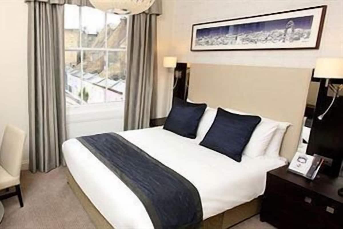 Ein Hotelzimmer mit Bett, Schreibtisch, Stuhl, Fernseher und einem Fenster mit Vorhängen.
