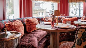 A cozy seating area with patterned cushions, a table set for dining, and a view of a historic building through large windows.