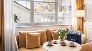 A room with a sofa, a table with a vase of flowers, a coffee cup, a plate with food, and a shopping bag.