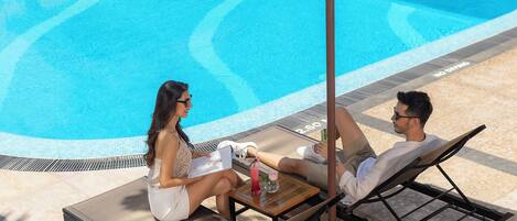 Una pareja descansando junto a una tumbona con una mesa, un sombrero y una bebida.
