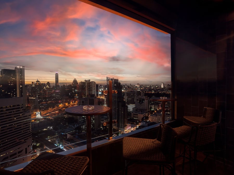 Vista panorámica de la ciudad desde un balcón, con rascacielos y un cielo al atardecer.