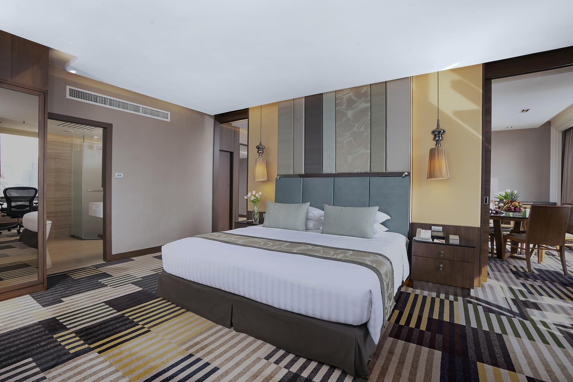A hotel room with a large bed, a desk, and a chair. There is a mirror on the wall and a window.