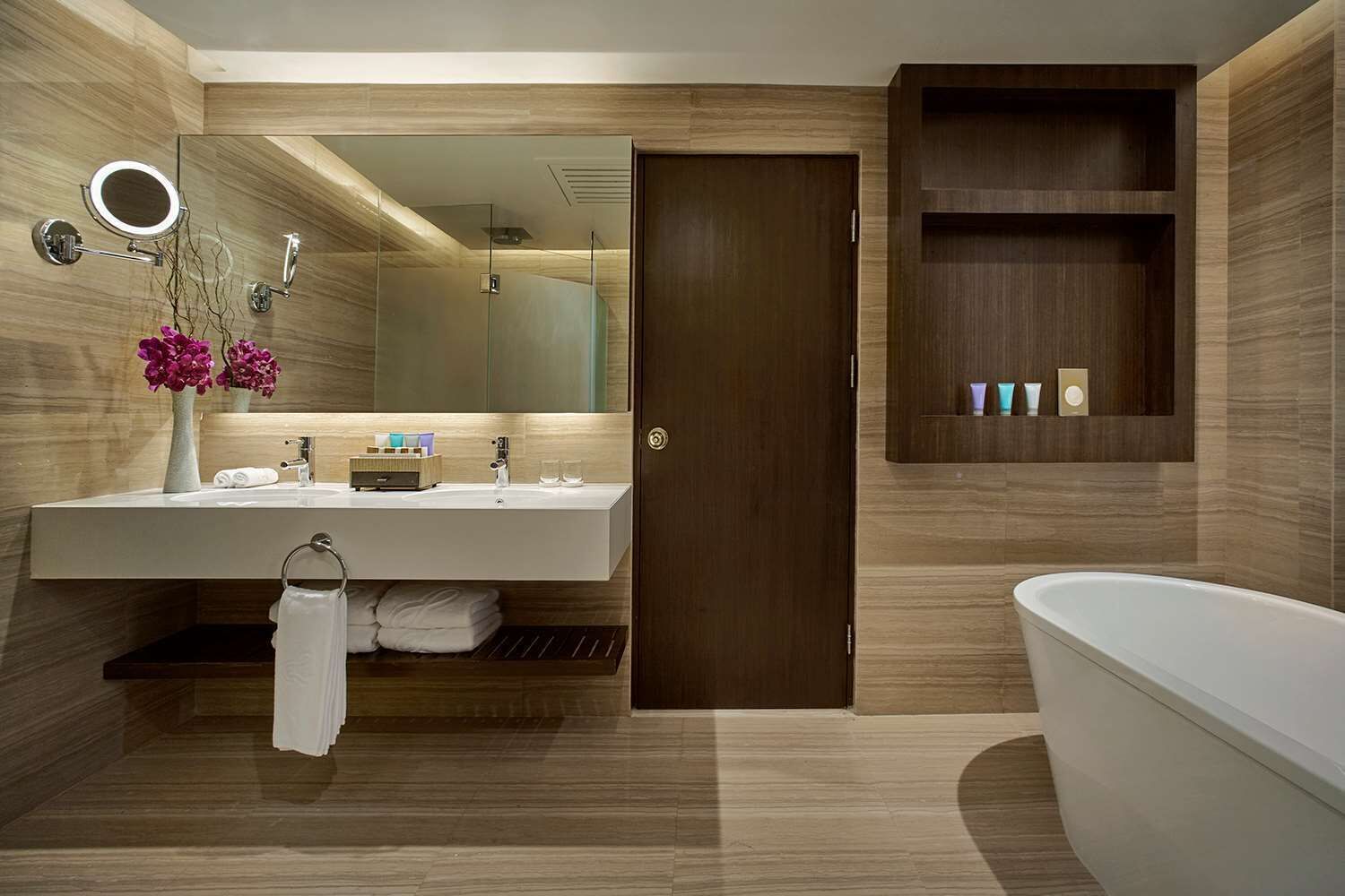 Een moderne badkamer met een grote spiegel, twee wastafels, een badkuip en een houten wastafelmeubel met een plank.