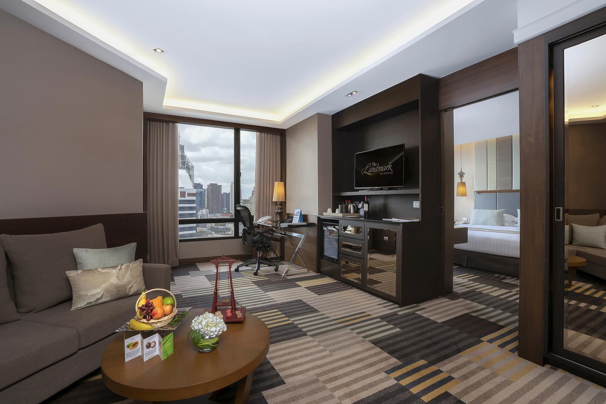 Ein modernes Hotelzimmer mit einer Couch, einem Essbereich, einer Küche und einem großen Fernseher.