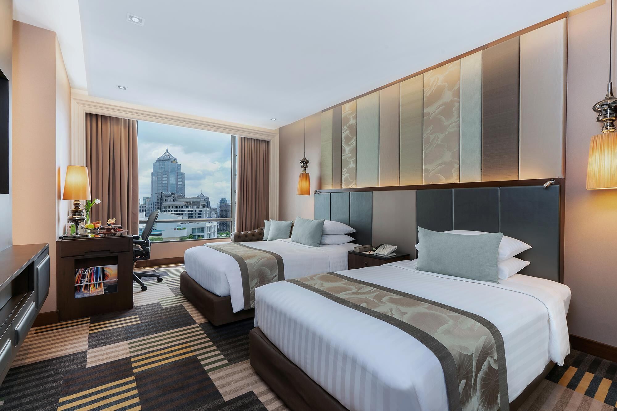 Een hotelkamer met twee bedden, een bureau en uitzicht op de stad.