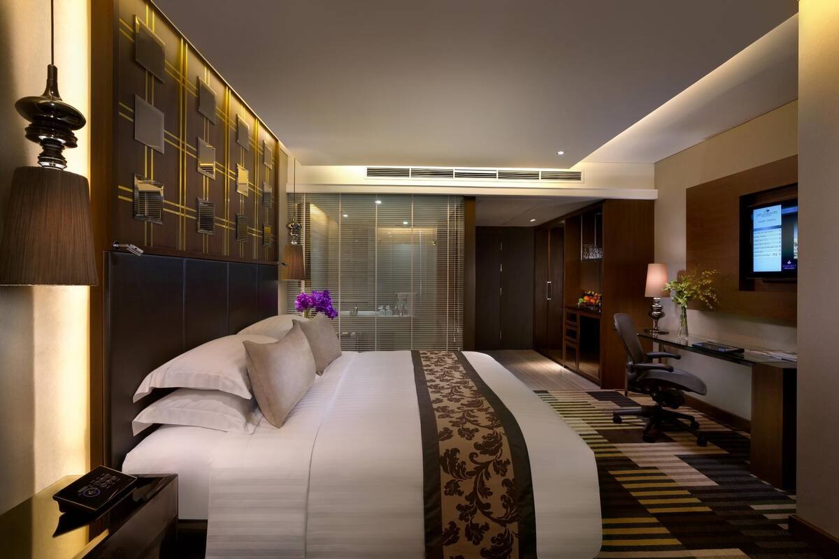 A modern hotel room with a large bed, a desk with a computer, and a TV mounted on the wall.