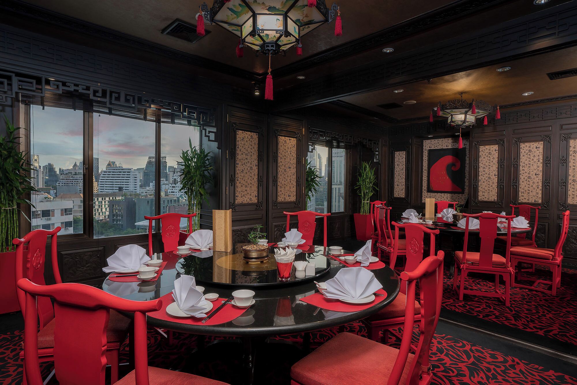 A dining area with red chairs and a round table, large windows with a city view, and traditional decor.
