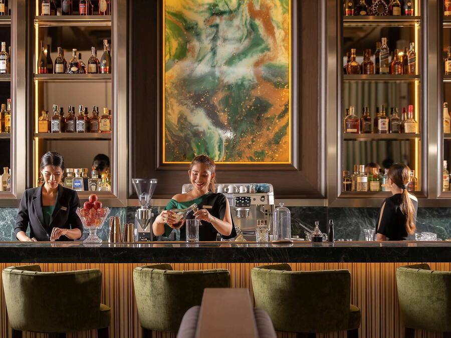 Uma área de bar com várias prateleiras de garrafas de bebidas, uma máquina de café e banquetas.