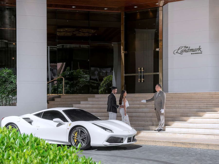 A white sports car parked in front of a building with a sign reading "The Landmark Bangkok."