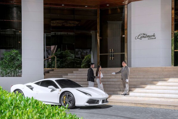 A white sports car parked in front of a building with a sign reading "The Landmark Bangkok."