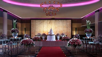A wedding reception hall with a central stage, floral arrangements, and a chandelier.