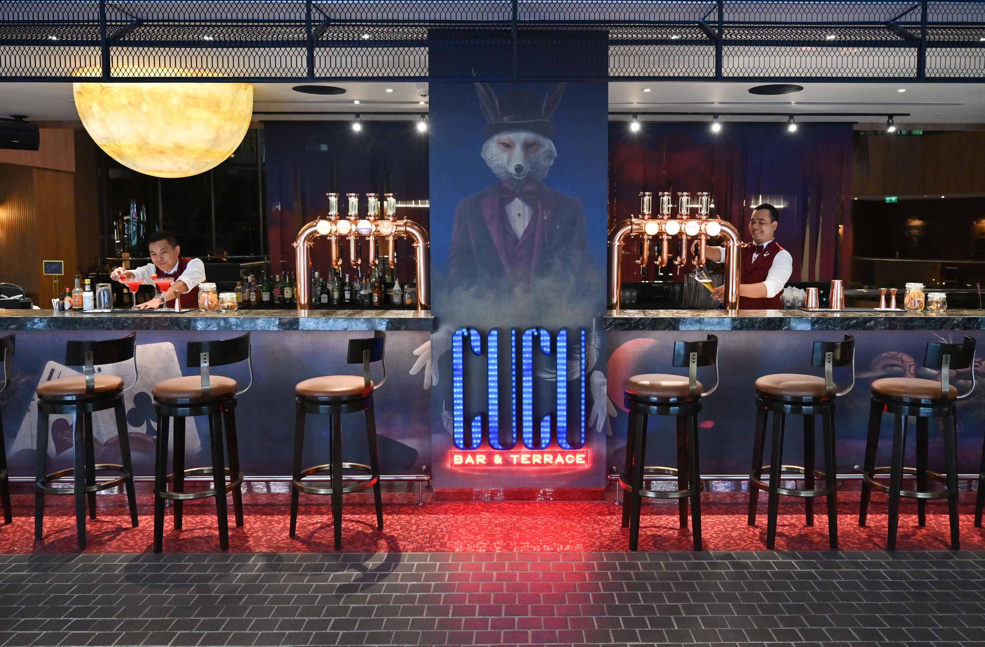 Eine Bar mit Hockern, einem Barkeeper und einer großen, beleuchteten Leuchtreklame.
