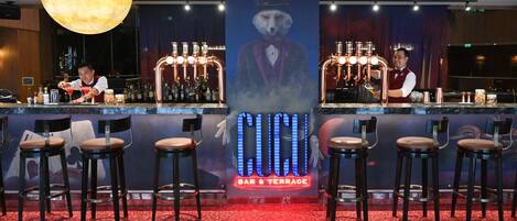 Zona de bar con taburetes, un barman y un letrero iluminado grande.