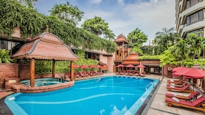 A swimming pool with lounge chairs and umbrellas, surrounded by lush greenery and traditional architecture. - The Landmark Bangkok (Bangkok)
