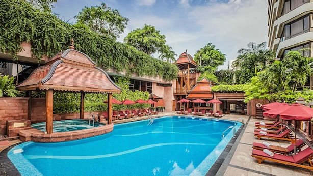 A swimming pool with lounge chairs and umbrellas, surrounded by lush greenery and traditional architecture. - The Landmark Bangkok (Bangkok)