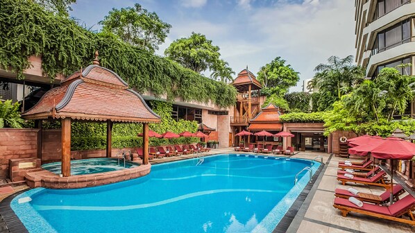 A swimming pool with lounge chairs and umbrellas, surrounded by lush greenery and traditional architecture. - The Landmark Bangkok (Bangkok)