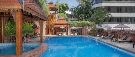 A swimming pool with a traditional pavilion, lounge chairs, and a multi-story building in the background.