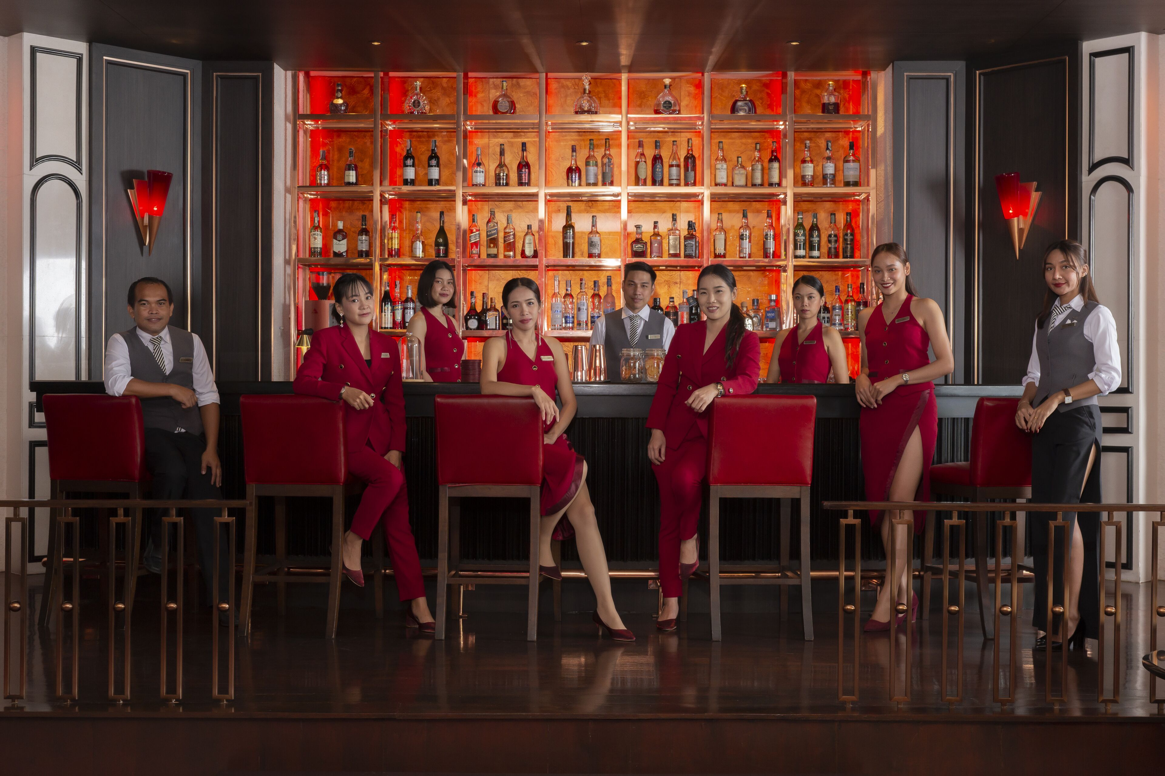 A bar area with a row of red bar stools and a bartender behind the bar.
