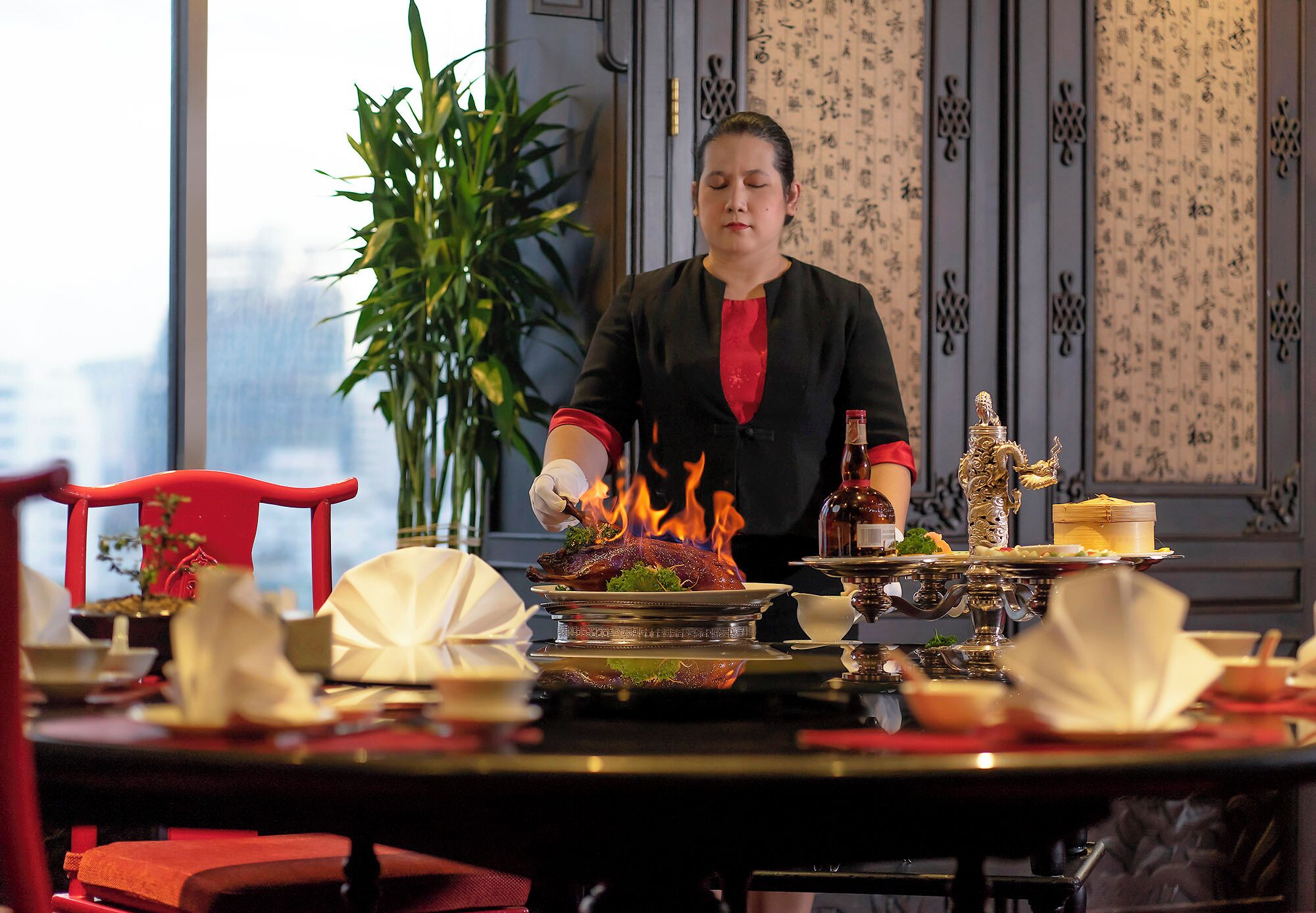 A dining table with a roasted duck centerpiece, a bottle, and a decorative statue.