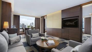A modern hotel room with a city view, a sofa set, a coffee table with books, and a TV mounted on the wall.