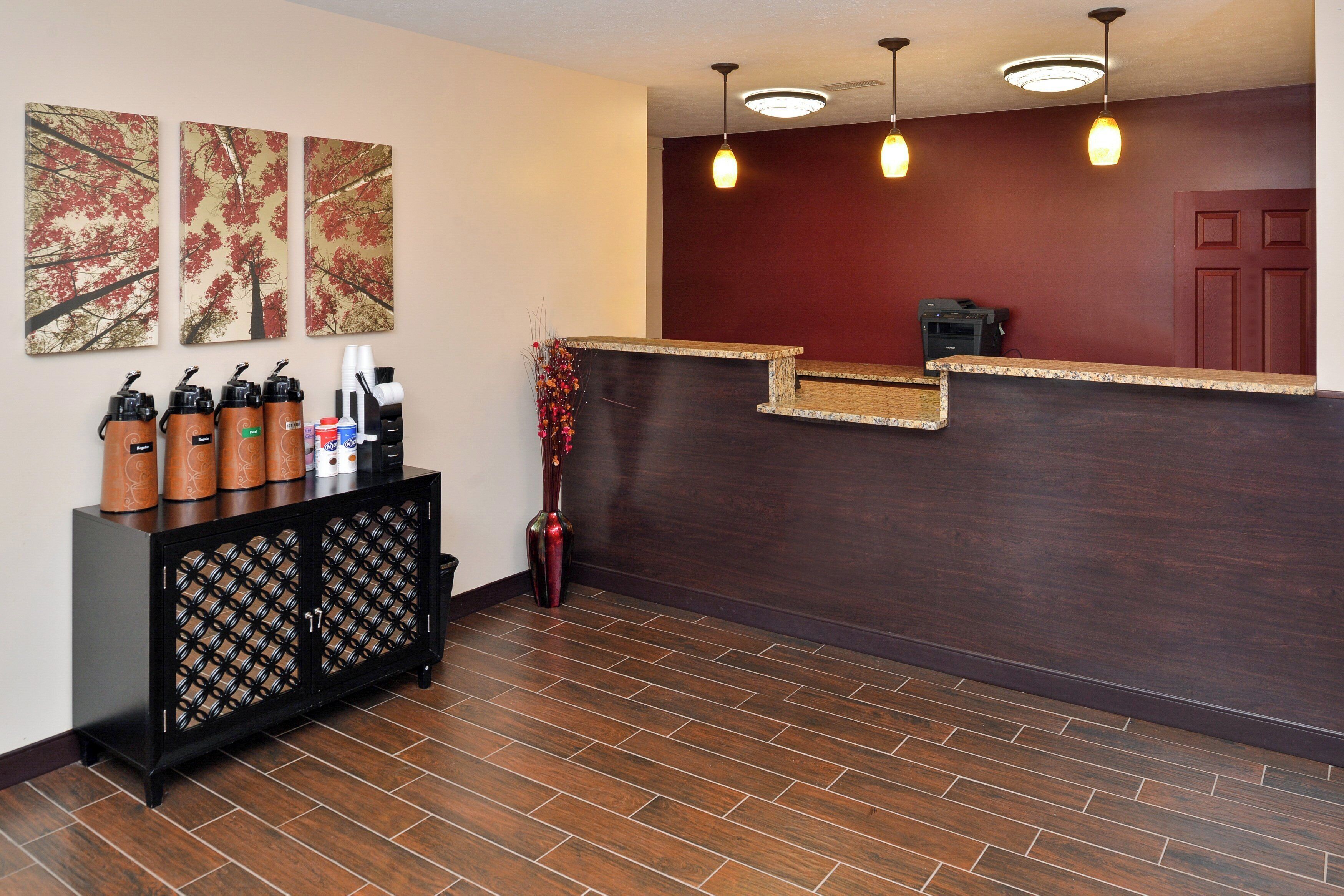 Un área de recepción con mostrador de madera oscura, una estación de café con dispensadores de la marca y tres obras de arte enmarcadas en la pared.