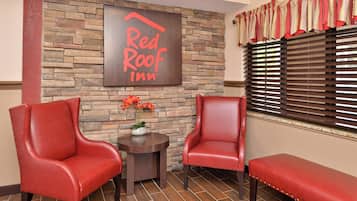 A Red Roof Inn lobby with two leather armchairs, a small table with a vase of flowers, and a bench.