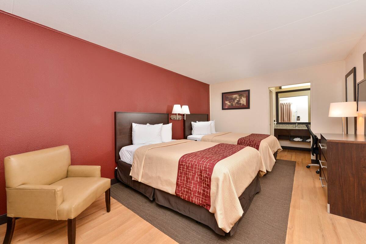 A hotel room with two beds, a desk, a chair, and a mirror.