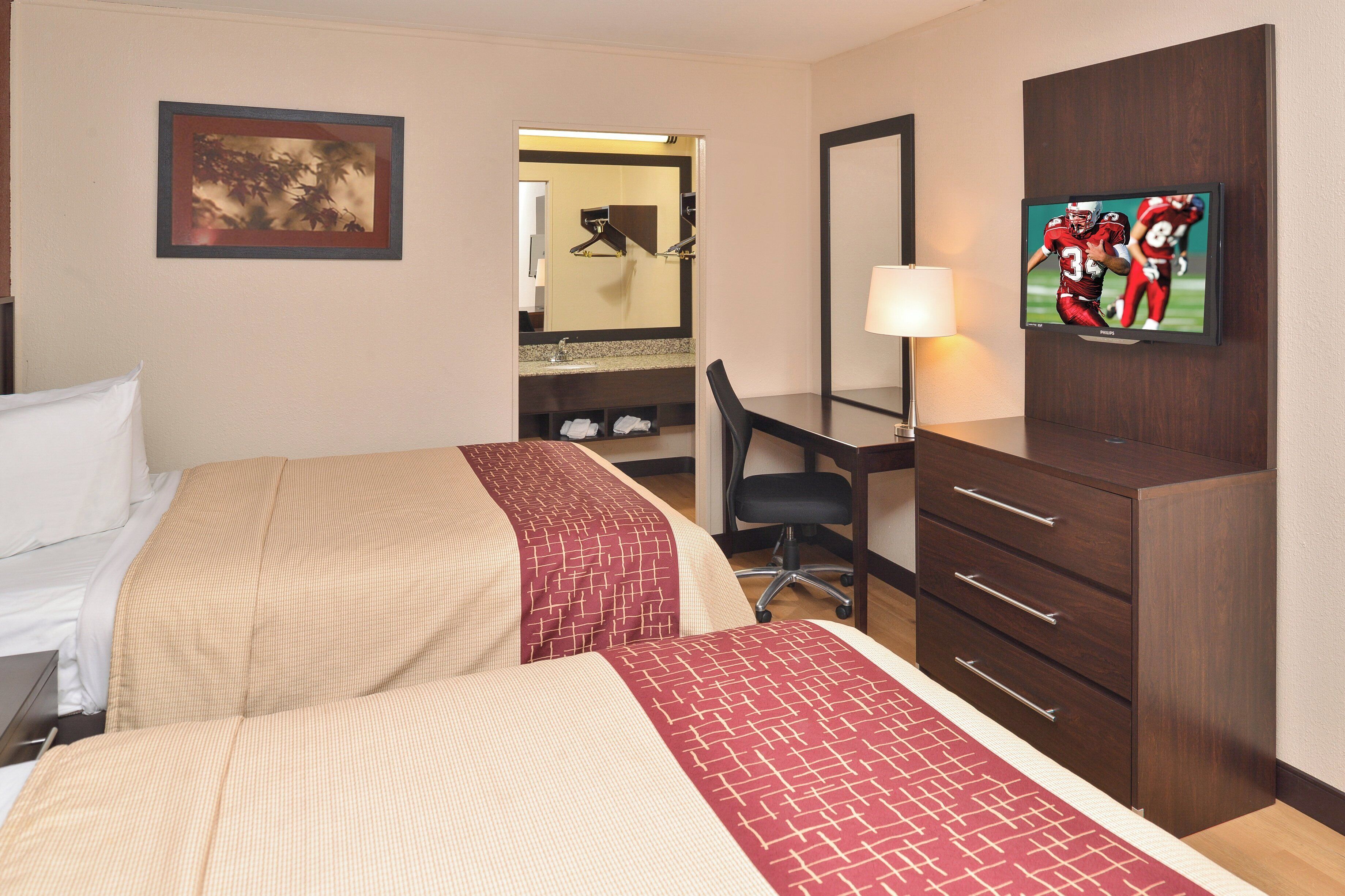 A hotel room with two beds, a desk, a chair, a TV, and a mirror.