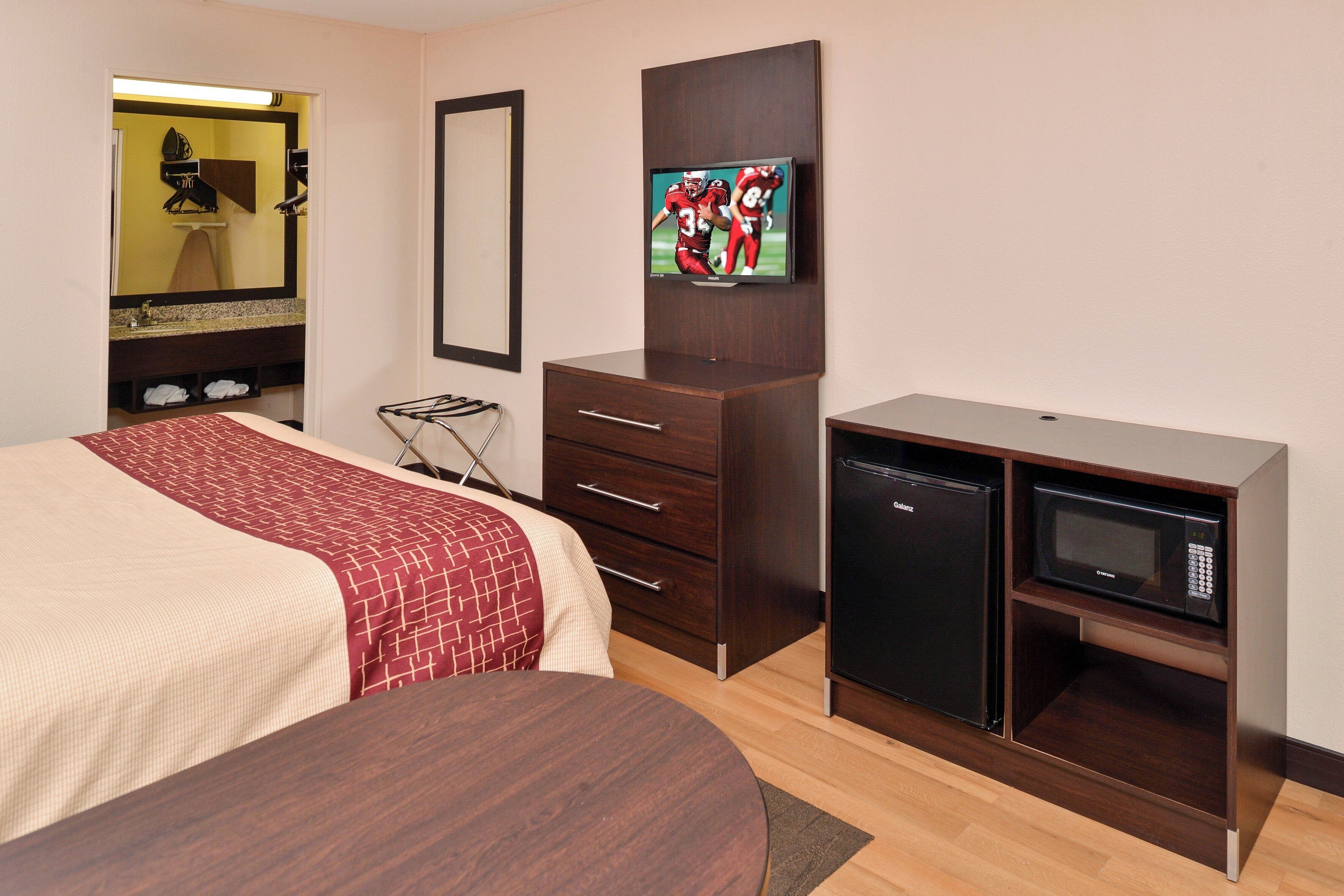 Una habitación de hotel con cama, cómoda, televisor y minibar.