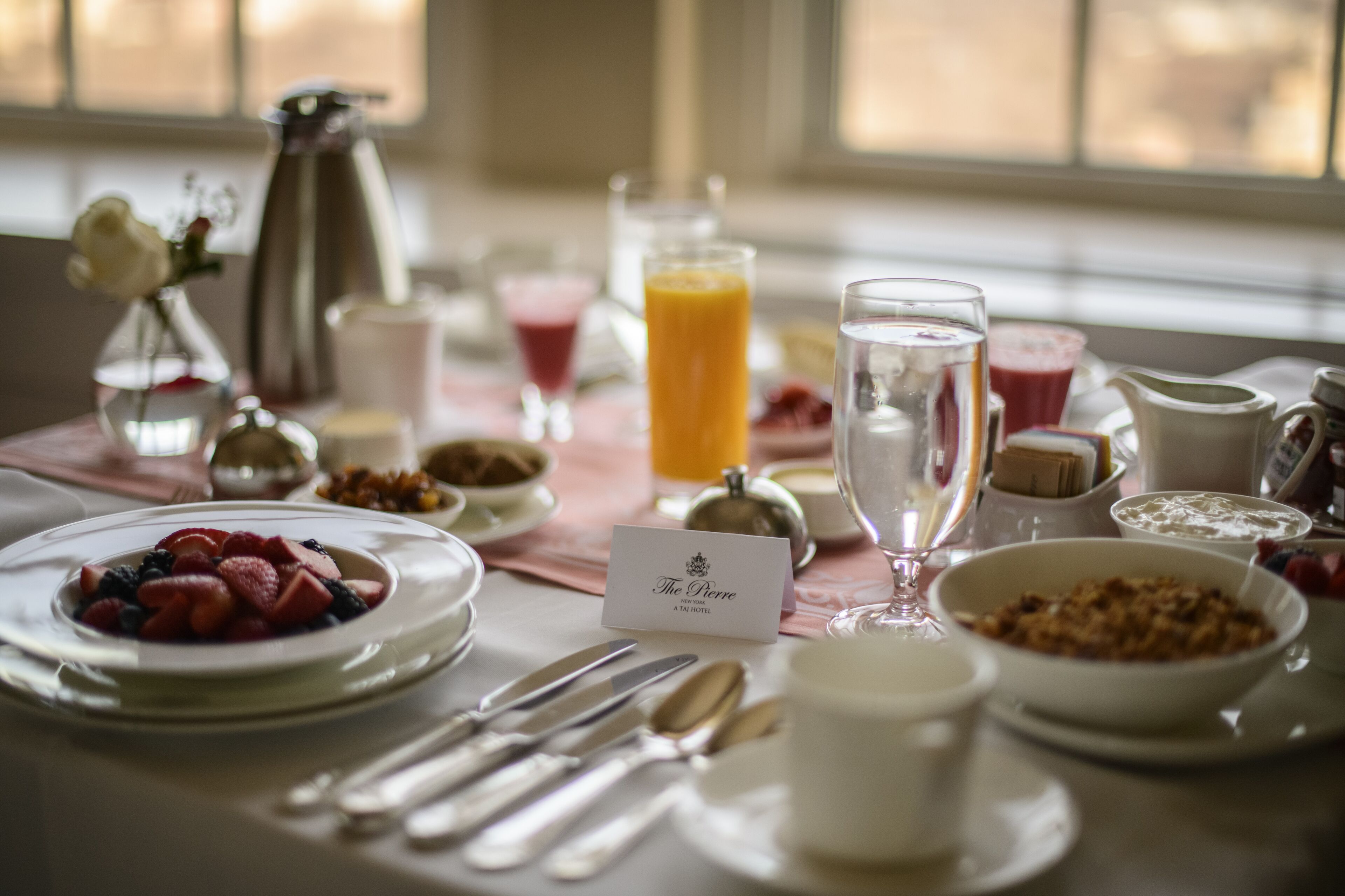 Une table de petit-déjeuner dressée avec divers plats, notamment des fruits, des céréales et des boissons, et une pancarte au centre portant l’inscription « The Pierre ».