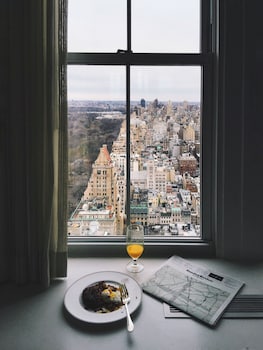 A living room with a view of a city skyline through large windows, a tufted sofa, and a patterned curtain. at The Pierre, A Taj Hotel, New York