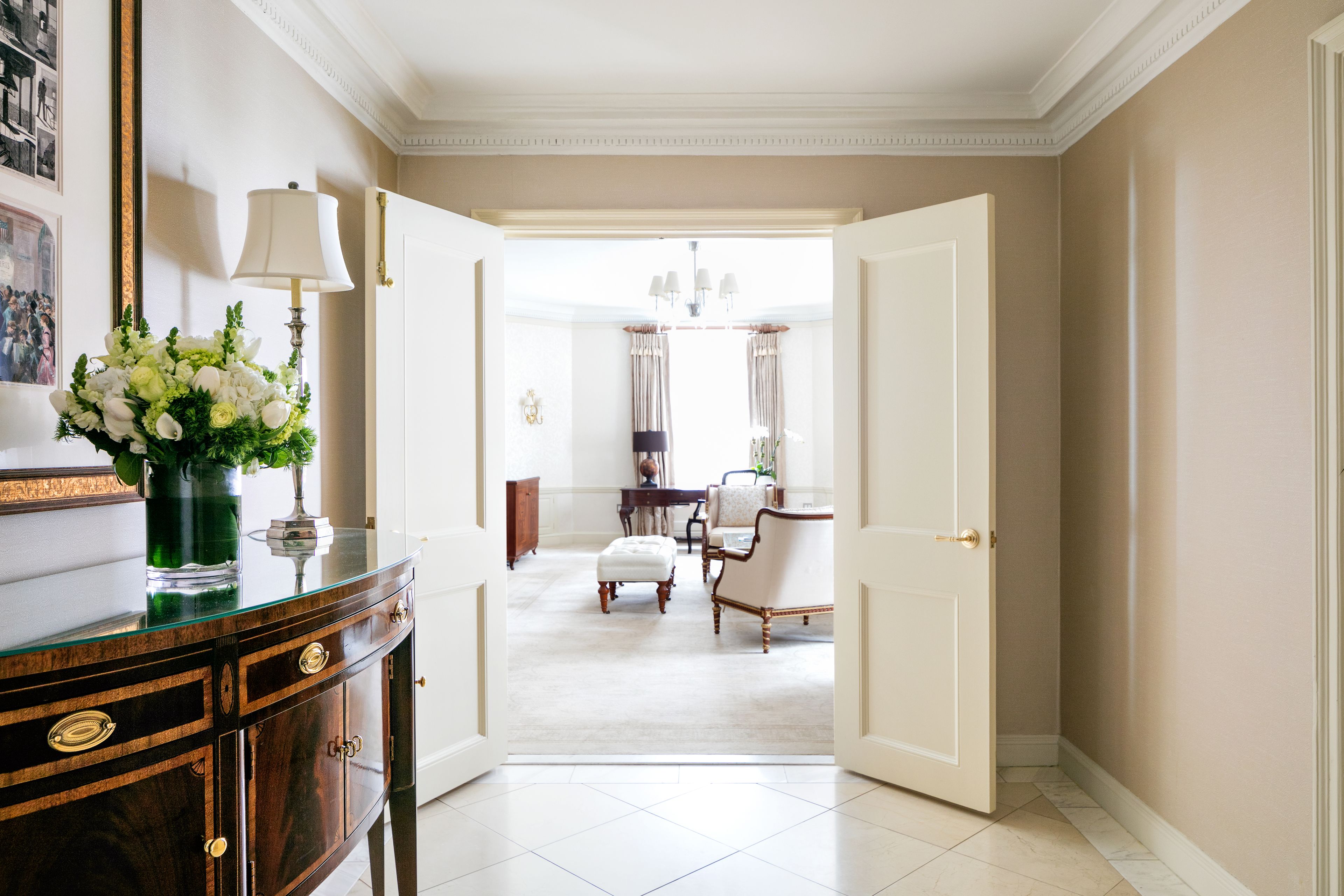 A hallway with a glass-top console table, a vase of flowers, and a door leading to another room.