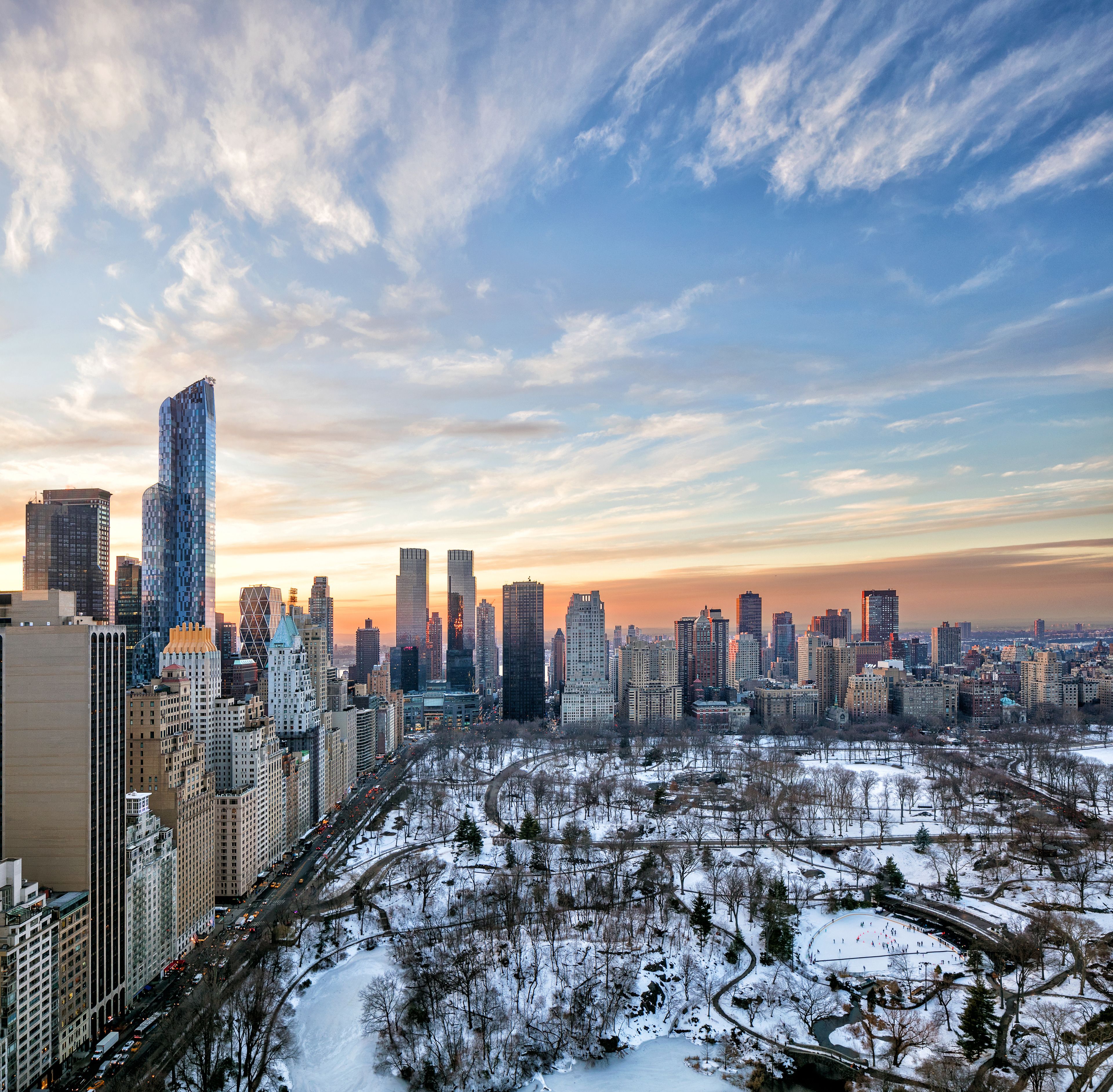 A cityscape with high-rise buildings and a snow-covered park with an ice rink.