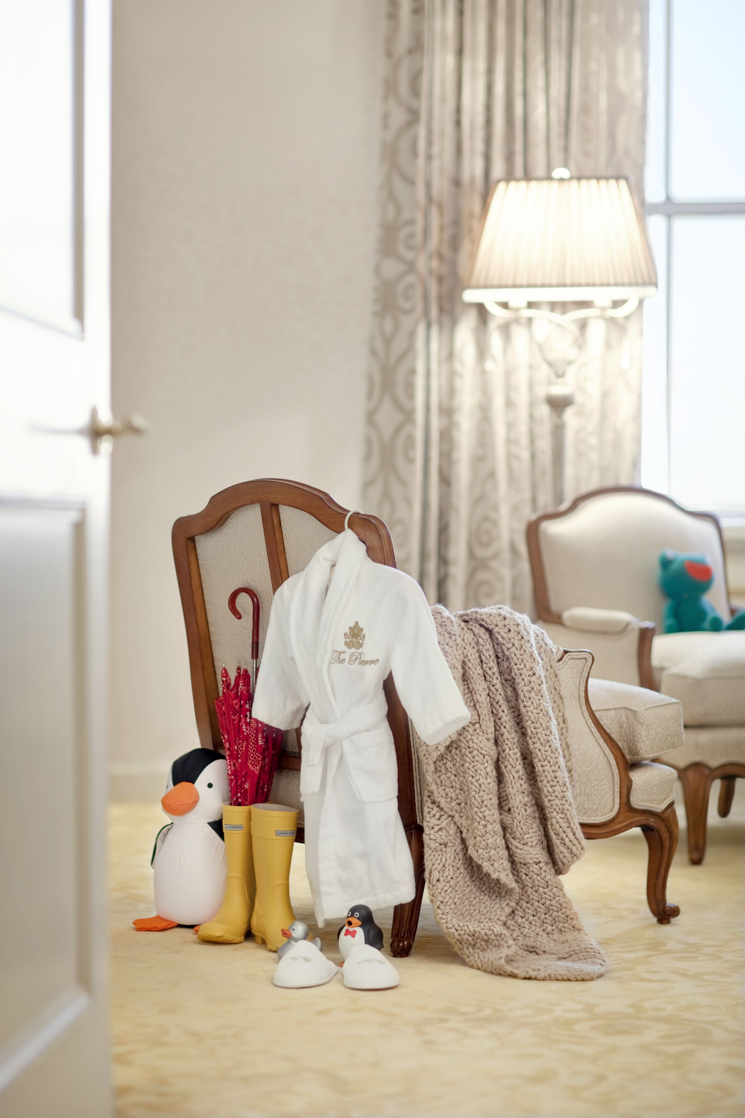 Une pièce comprenant une chaise en bois, une lampe et un porte-manteau sur lequel est posé un peignoir blanc et une couverture.
