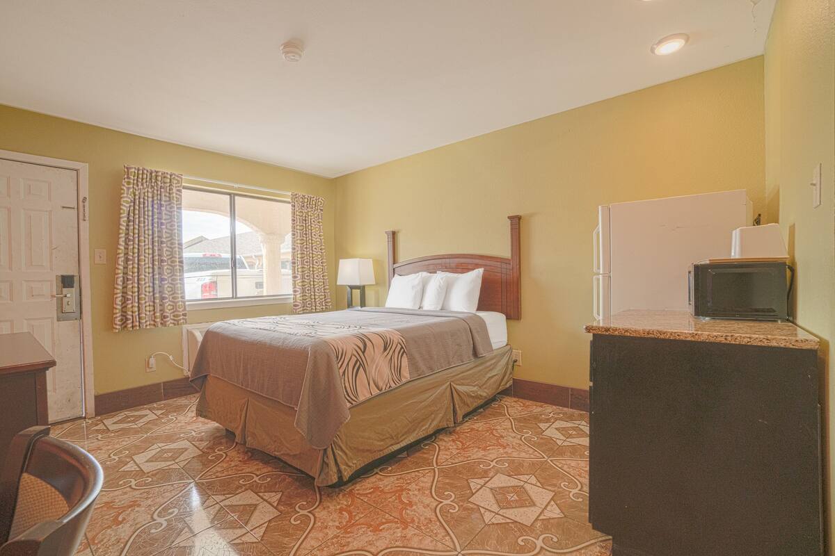 A hotel room with a bed, a desk, a refrigerator, and a window with curtains.