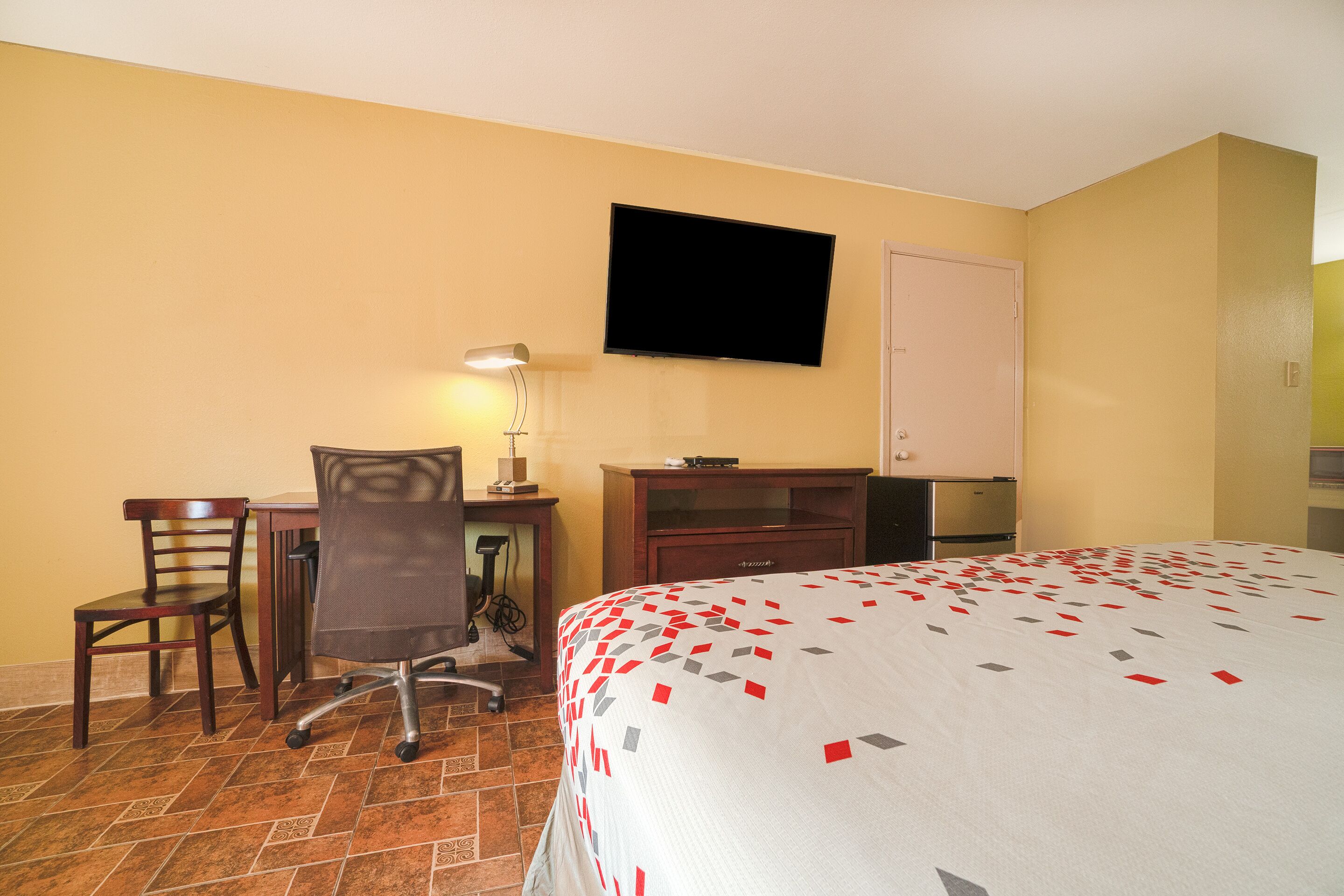 A hotel room with a bed, desk, chair, television, and a cabinet.