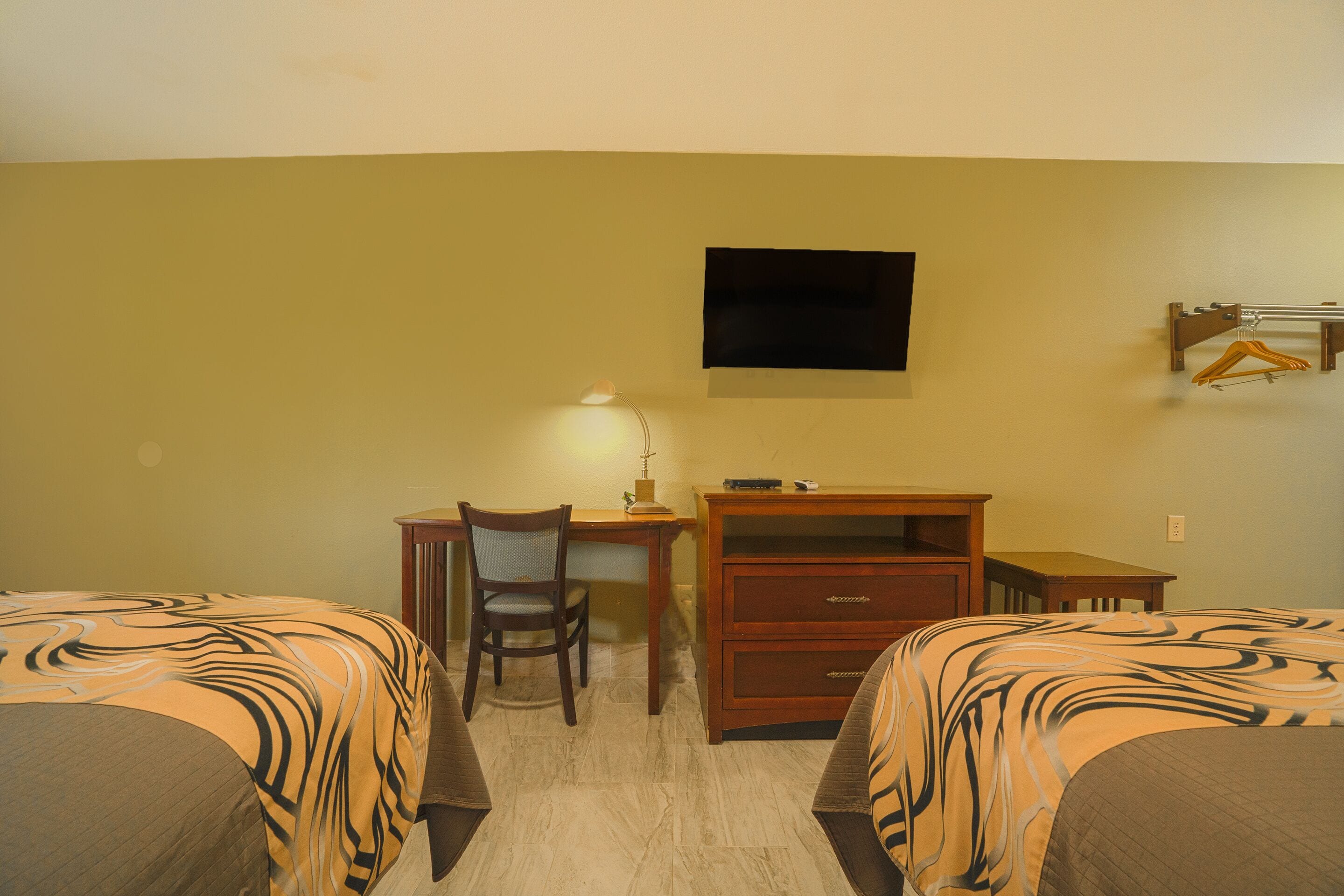 A hotel room with two beds, a desk, a chair, a TV mounted on the wall, and a small table.