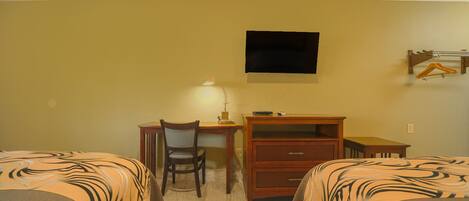 A hotel room with two beds, a desk, a chair, a TV mounted on the wall, and a small table.