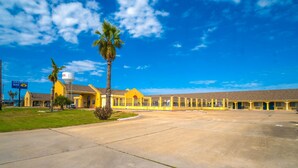 A motel with a large parking lot, a palm tree, and a water tower. - Aransas Bay Inn & Suites Corpus Christi by OYO (Aransas Pass)