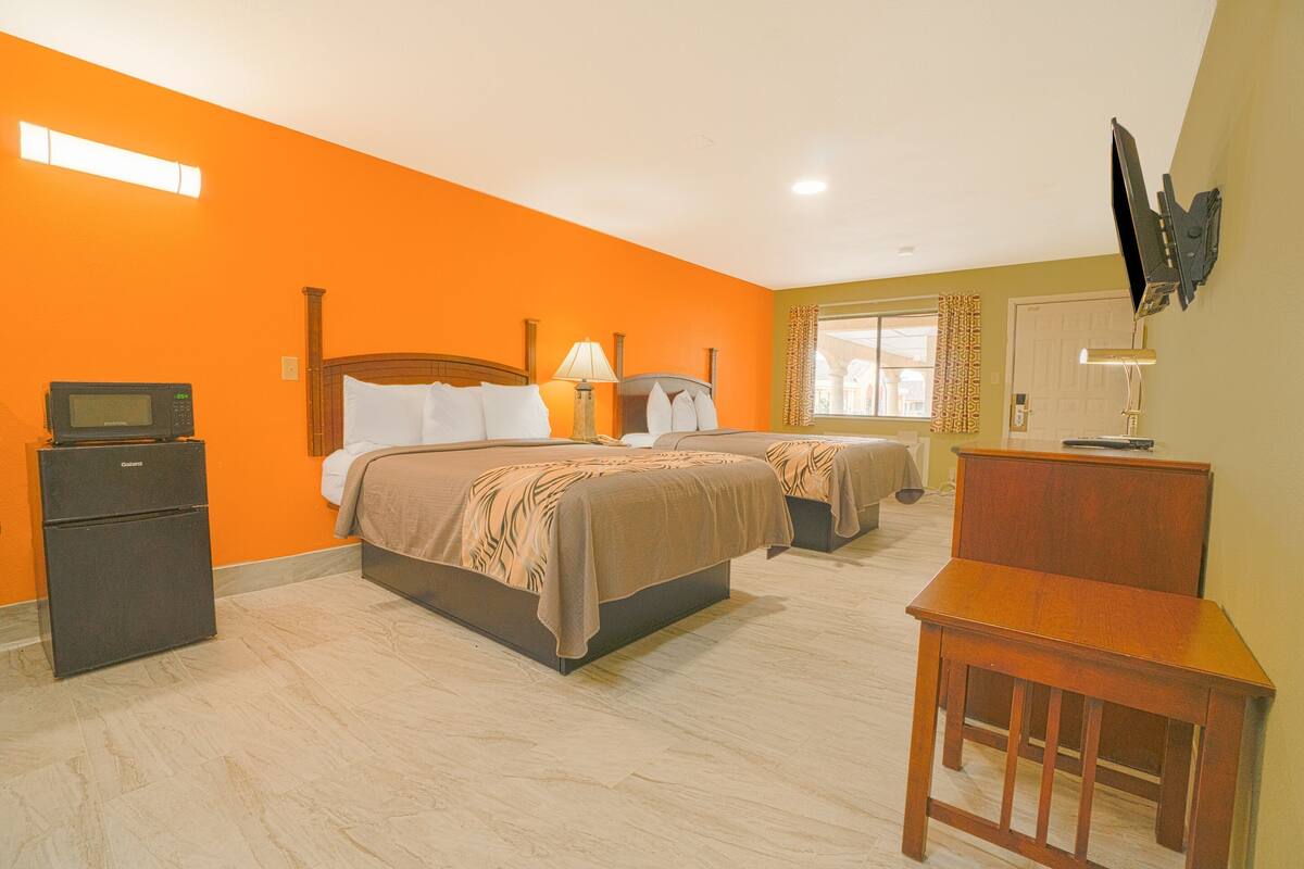 A hotel room with two beds, a desk, a TV, a microwave, and a window with curtains.