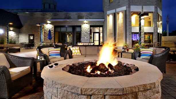 An outdoor seating area with a stone fire pit, wicker furniture, and a building in the background. - DoubleTree by Hilton Denver - Thornton (Thornton)