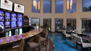 A bar area with a curved counter, multiple seating options, and large windows offering views of the sky. - DoubleTree by Hilton Denver - Thornton (Thornton)