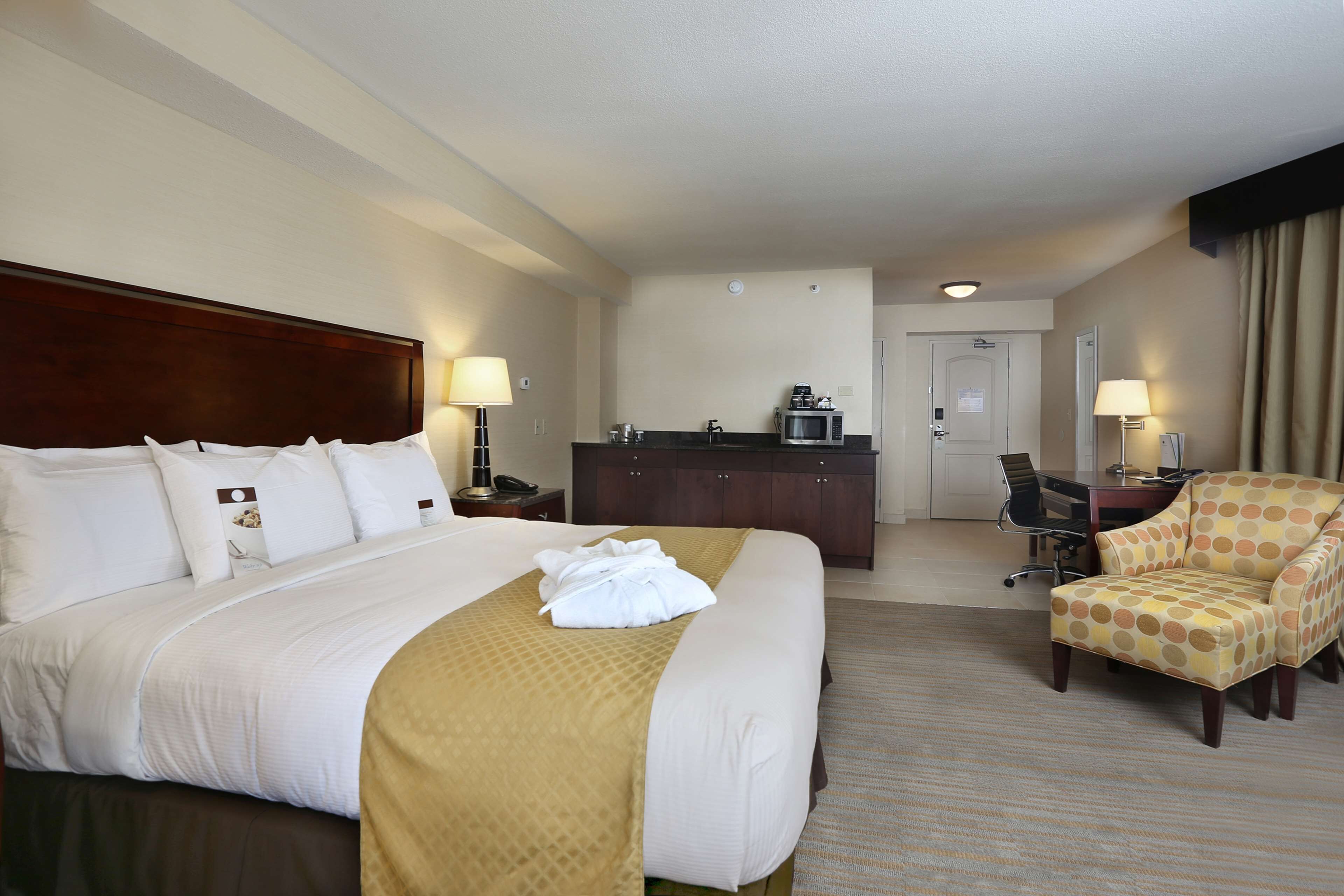A hotel room with a large bed, a desk with a computer, a chair, and a microwave.