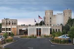 Un hotel DoubleTree con fachada de ladrillo moderno, una entrada central y un área de estacionamiento con varios coches.