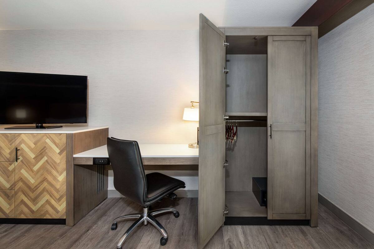 A modern room with a wooden desk, a black office chair, a television, and a wardrobe with a mirror.