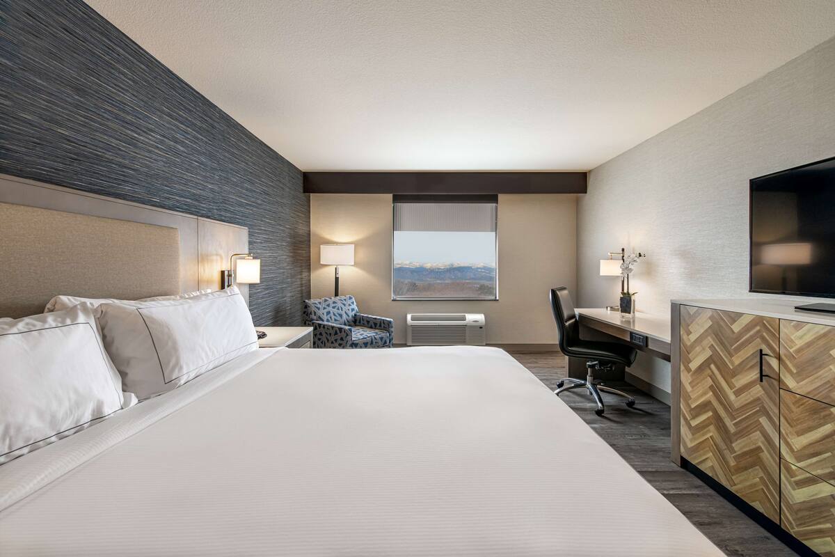 A hotel room with a large bed, a desk, a chair, a television, and a window with a mountain view.
