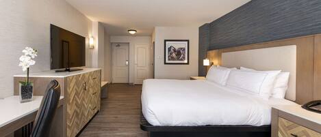 A hotel room with a bed, bedside table, desk, chair, and a TV.