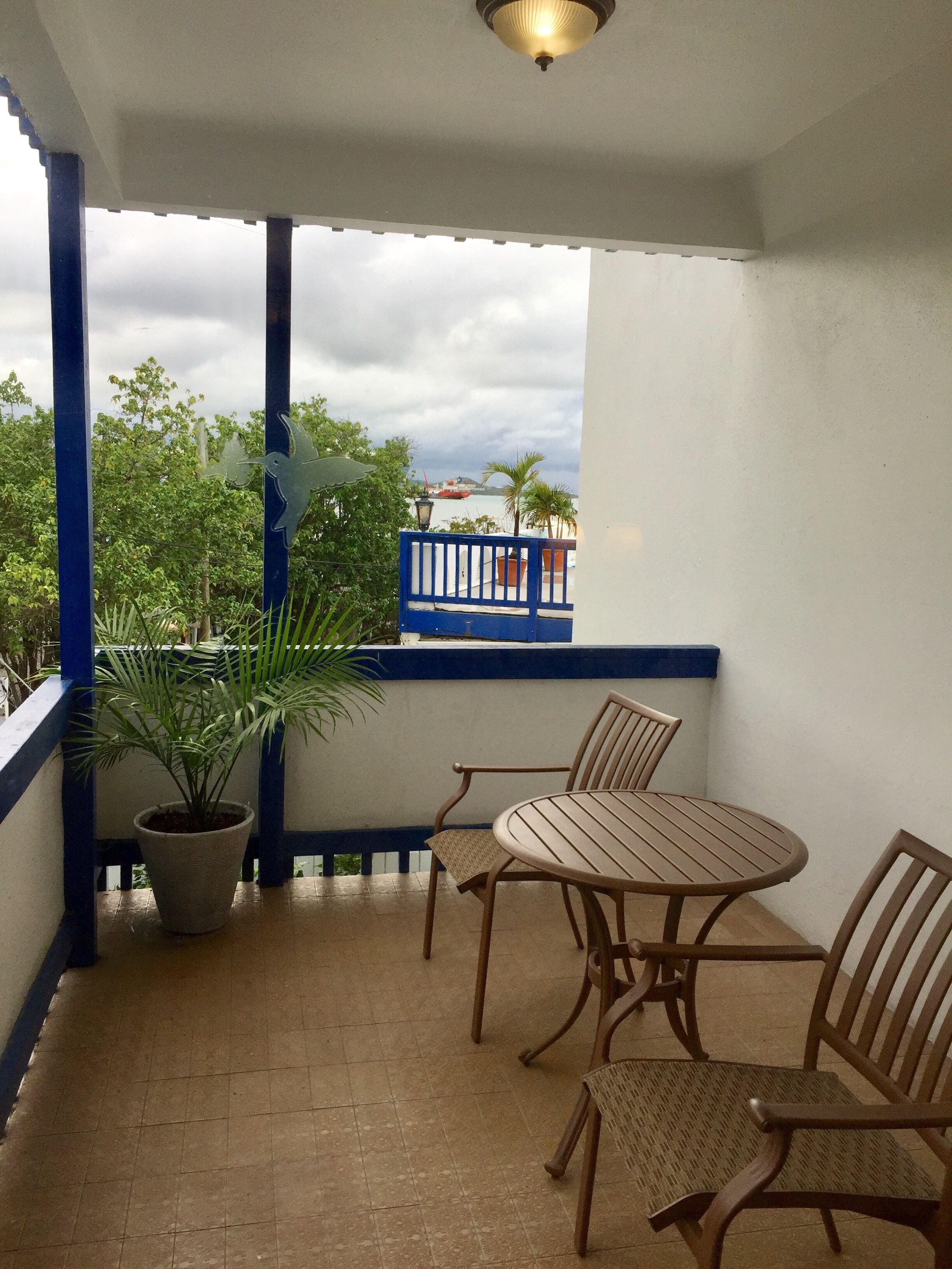Varanda com mesa e cadeiras, um vaso de planta e vista para o mar e um barco vermelho.